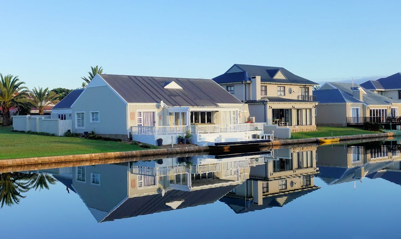 cta-02 Luxury modern homes reflecting on a peaceful, clear lake during daylight, showcasing architectural beauty.