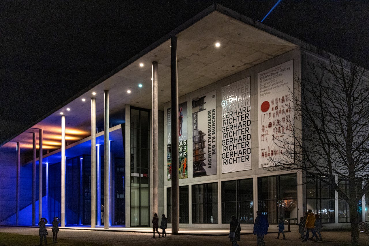 gallery-01 Night view of Pinakothek der Moderne in Munich with colorful lighting and visitors.