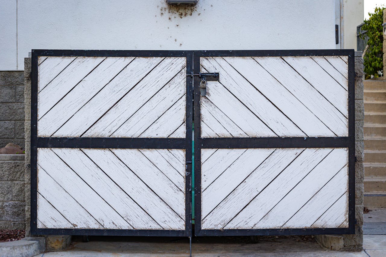 about-01 A rustic white wooden gate with diagonal panels and a black metal frame in a residential entrance.